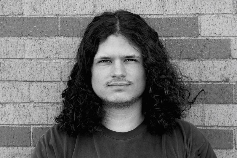 Black and white photo of a young man with long curly hair.
